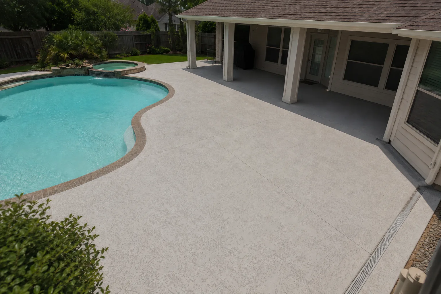 Beige spray-texture pool deck with a deck drain beside a covered patio